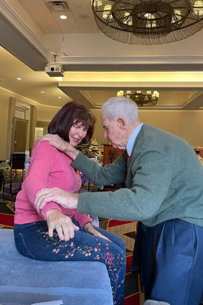 Geoffrey Morell at hotel event healing woman in pink sweater with Clendenning Technique